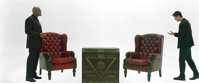 Still from the movie The Matrix with Morpheus and Neo in a white room with two armchairs and a television set